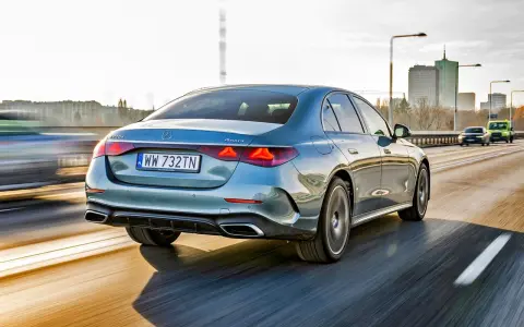 Elegancki, błękitny Mercedes E220d 4MATIC pędzi autostradą, mijając miejską panoramę.