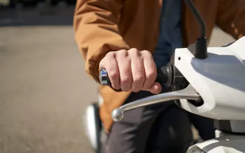 Dłoń trzymająca kierownicę skutera elektrycznego. Może to być związane z dopłatą do skutera elektrycznego.