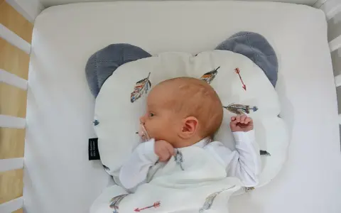 Nowe niemowlę śpi na poduszce w kształcie misia, otulone kocykiem z piórkami. Czy niemowlę może spać na poduszce? Bezpieczeństwo przede wszystkim!