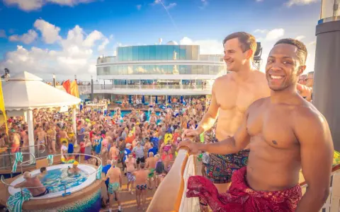 Two men smile on a cruise deck, surrounded by a lively crowd enjoying a pool party. These scenes are typical of positive gay cruises reviews.