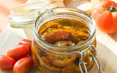 Bocal de tomates séchées à l'huile d'olive, avec des tomates fraîches à côté.