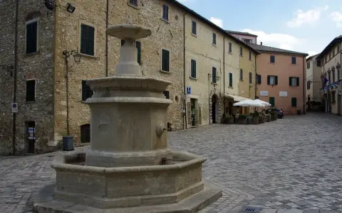 Piazza con fontana in pietra, circondata da edifici storici. Un angolo di pace nei borghi vicino Cattolica.
