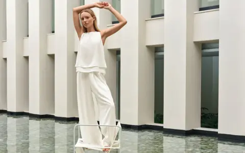 Frau in weißem Outfit mit weiten Palazzo Hosen, elegant gestylt vor moderner Architektur.