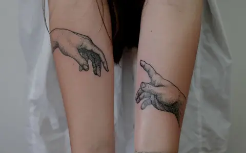 Dwa tatuaże dłoni, jakby sięgały ku sobie, symbolizujące ochronę przed złem i połączenie.