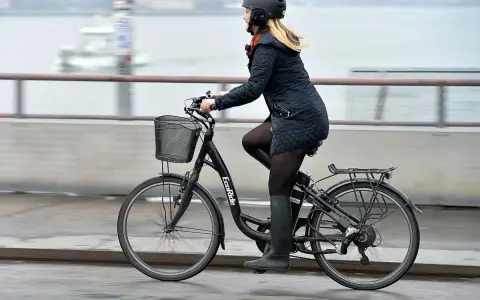 Kvinna cyklar på en elcykel, kanske med bidrag för att underlätta pendlingen. Hon bär hjälm och en varm jacka.