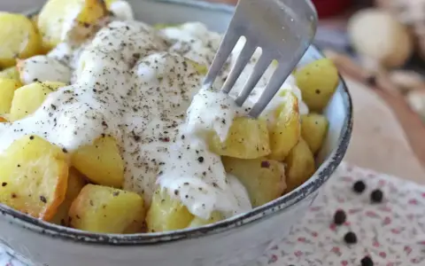 Ziemniaki w kremowym sosie z pieprzem, inspirowane przepisem Cacio e Pepe. Widok z bliska na widelec nabijający ziemniaka.
