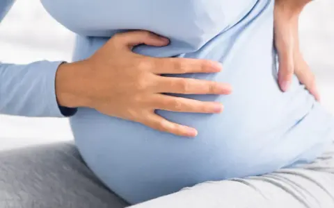 Kobieta w ciąży trzyma się za bok, odczuwając ból. Może to być kolka nerkowa w ciąży.