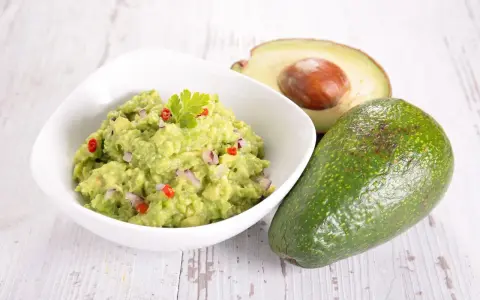 Miseczka guacamole z awokado, cebulą i papryczką chili na drewnianym tle.
