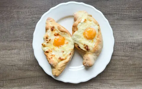 Dwa chaczapuri adżarskie z jajkiem i serem na białym talerzu. Idealne na szybki obiad, gdy masz ochotę na chaczapuri przepis.
