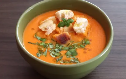 Aksamitna keto zupa pomidorowa z grzankami i świeżą bazylią w zielonej misce.