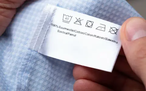 Metka z symbolami prania: prać w 40°C, nie wybielać, prasować, nie wirować symbol. 100% bawełna.
