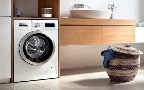 Lavadora blanca moderna lista para instalar en un baño con cesta de ropa sucia.