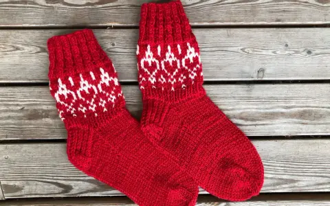 Två par röda, stickade strumpor med vitt mönster av hjärtan och snöflingor ligger på en träbänk. Perfekta för kalla dagar!