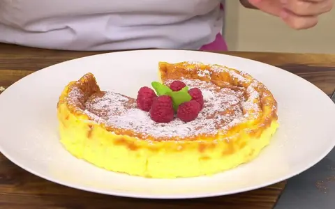 Tarta de queso Arguiñano recién horneada, espolvoreada con azúcar glas y decorada con frambuesas y menta.