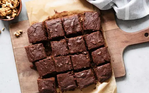 Brownies au chocolat coupés en carrés sur une planche en bois, accompagnés de noix. Un délicieux dessert healthy.