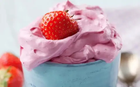 Puszysty, różowy krem z mascarpone z truskawką na wierzchu, podany w niebieskim naczyniu.