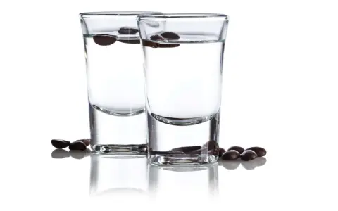 Zwei Gläser mit klarem Schnaps, darin schwimmende Kaffeebohnen. Der Sambuca-Prozent ist hier gut sichtbar.