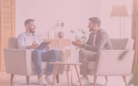 Rozmowa dwóch mężczyzn w przytulnym gabinecie. Jeden z nich, trzymający teczkę, wydaje się wyjaśniać, jak zostać terapeutą uzależnień.