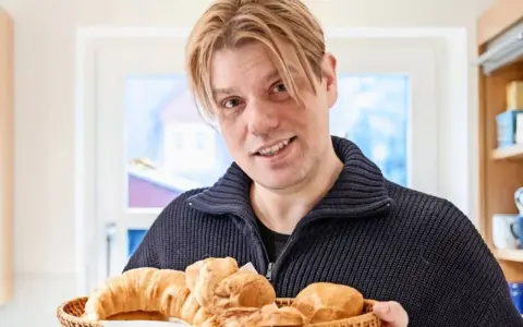 Mann mit blonden Haaren hält einen Korb mit frischen Backwaren, darunter ein Croissant und ein Kieler Semmel.