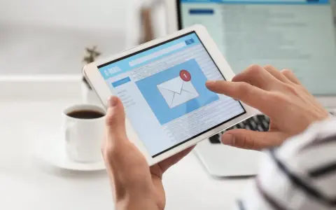 Ręce trzymają tablet z ekranem poczty e-mail, gdzie widać powiadomienie o nowej wiadomości. Może to być początek pisania reklamacji po angielsku.