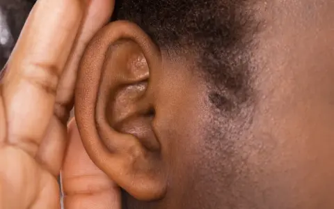 Une main couvre une oreille, comme pour mieux entendre ou se protéger du bruit. Cela peut évoquer ce qu'est-ce qui provoque des acouphènes.