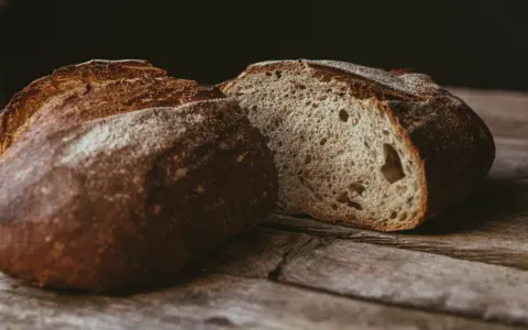 Ein rustikales, aufgeschnittenes sauerteigbrot ohne kneten liegt auf einer Holzoberfläche. Die Kruste ist dunkelbraun und knusprig, das Innere luftig und porös.