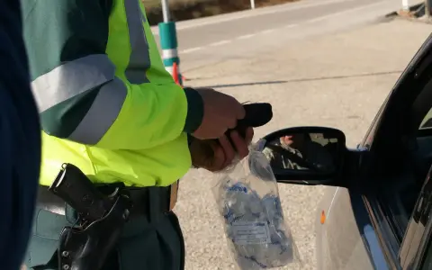 Policjant w kamizelce odblaskowej trzyma alkomat i worek z ustnikami przy samochodzie.