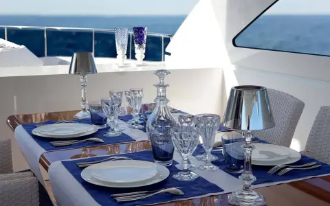 Emplacement des couverts sur une table dressée sur un yacht, avec des verres en cristal, une carafe et des lampes.