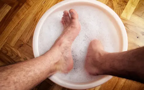 A person's feet soaking in a bubbly foot bath on a wooden floor.