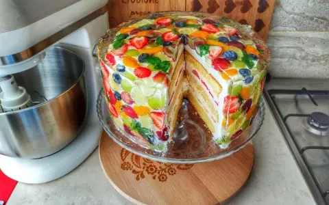 Kolorowy tort z owocami w żelu, z kawałkiem wyciętym, prezentuje się apetycznie.