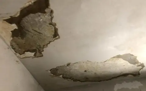 Zalany sufit z odpadającym tynkiem. Widać ciemne plamy i uszkodzenia, świadczące o przecieku.