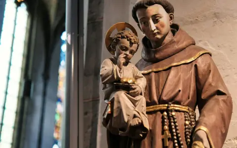 A statue shows what friars wear: brown robes, a cord belt, and a rosary. A child with a halo holds fruit.