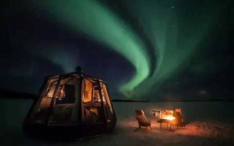 Drömmen att bo i igloo och se norrsken blir verklighet. En glaskupol med säng och en mysig eldstad utomhus under en magisk himmel.