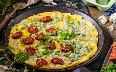 Pyszny omlet na słono z kawałkami chorizo i niebieskim serem, posypany szczypiorkiem i natką pietruszki.