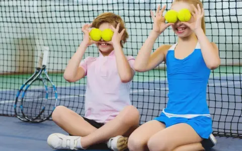 Bambini che fanno sport, con palline da tennis sugli occhi, ridono su un campo da tennis.