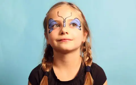 Ein Mädchen mit einem Schmetterling, der leicht geschminkt ist, lächelt.
