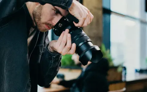 Mężczyzna z brodą w czarnej kurtce trzyma aparat, gotowy do uchwycenia chwili w stylu street photography.