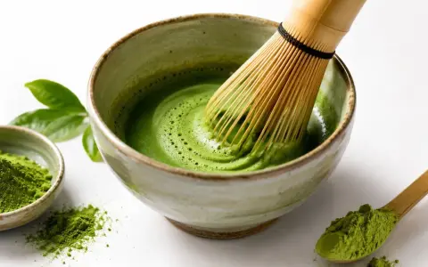 Przygotowanie idealnego matcha: zielony proszek, bambusowa miotełka i spieniony napój w miseczce.