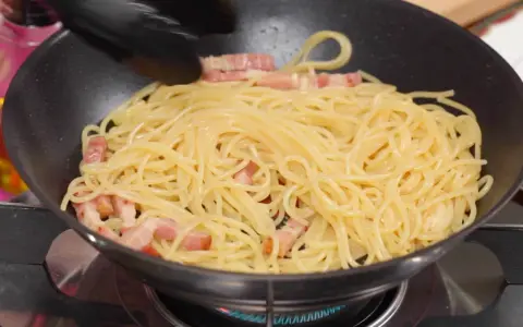 Espaguetis con trozos de panceta en una sartén, preparándose para unos deliciosos tallarines a la carbonara.