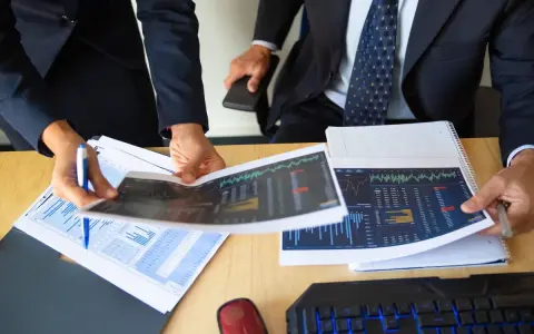 Dos personas analizan gráficos financieros, discutiendo los diferentes tipos de auditorías y sus implicaciones para el negocio.