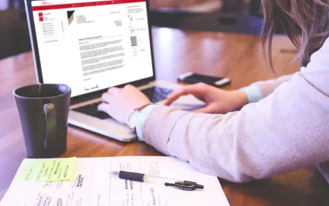 Kobieta pisze list motywacyjny bez doświadczenia na laptopie, obok kubek kawy i notatki.