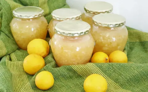 Plusieurs bocaux de confiture de citron maison, entourés de citrons frais, sur un tissu vert rayé.