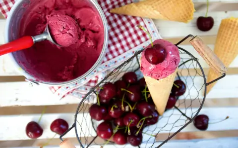 Ein Eisbecher mit Kirscheis, eine Kugel in einer Waffel, frische Kirschen und leere Waffeln.