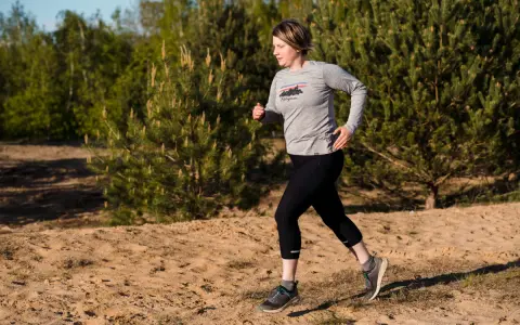 Frau beim **trail running** auf sandigem Untergrund, umgeben von Kiefern und Bäumen.