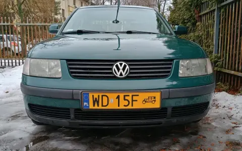 Zielony Volkswagen z żółtą tablicą rejestracyjną na tle płotu i śniegu.