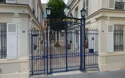 Brama do Ecole de Paris, ozdobiona złotymi detalami, prowadzi na dziedziniec z drzewem i ławką.
