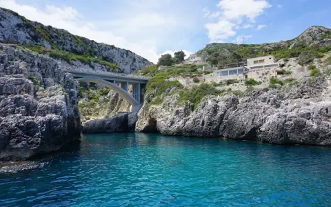Ponte moderno su un mare cristallino, incastonato tra scogliere rocciose. Un luogo magico dove si incontrano i due mari in Puglia, con un ristorante panoramico sulla collina.