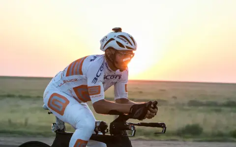 Cyclist in aerodynamic gear races across America at sunset, pushing through the vast landscape.