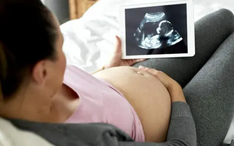 Kobieta w ciąży ogląda na tablecie zdjęcie USG. To jej badania prenatalne w 3 trymestrze.