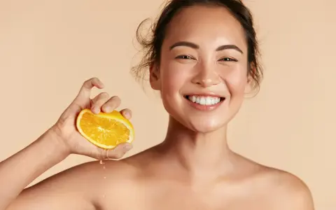 Donna sorridente con fetta d'arancia, suggerisce che il siero alla vitamina C si può usare in estate per una pelle luminosa.